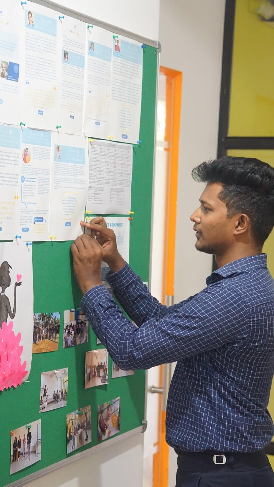 Employee curating Tekvocation’s workplace bulletin board with team updates, creative contributions, and workshop visuals.